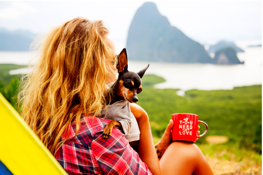 Woman and her dog outside drinking coffee, looking at the mountains and lake