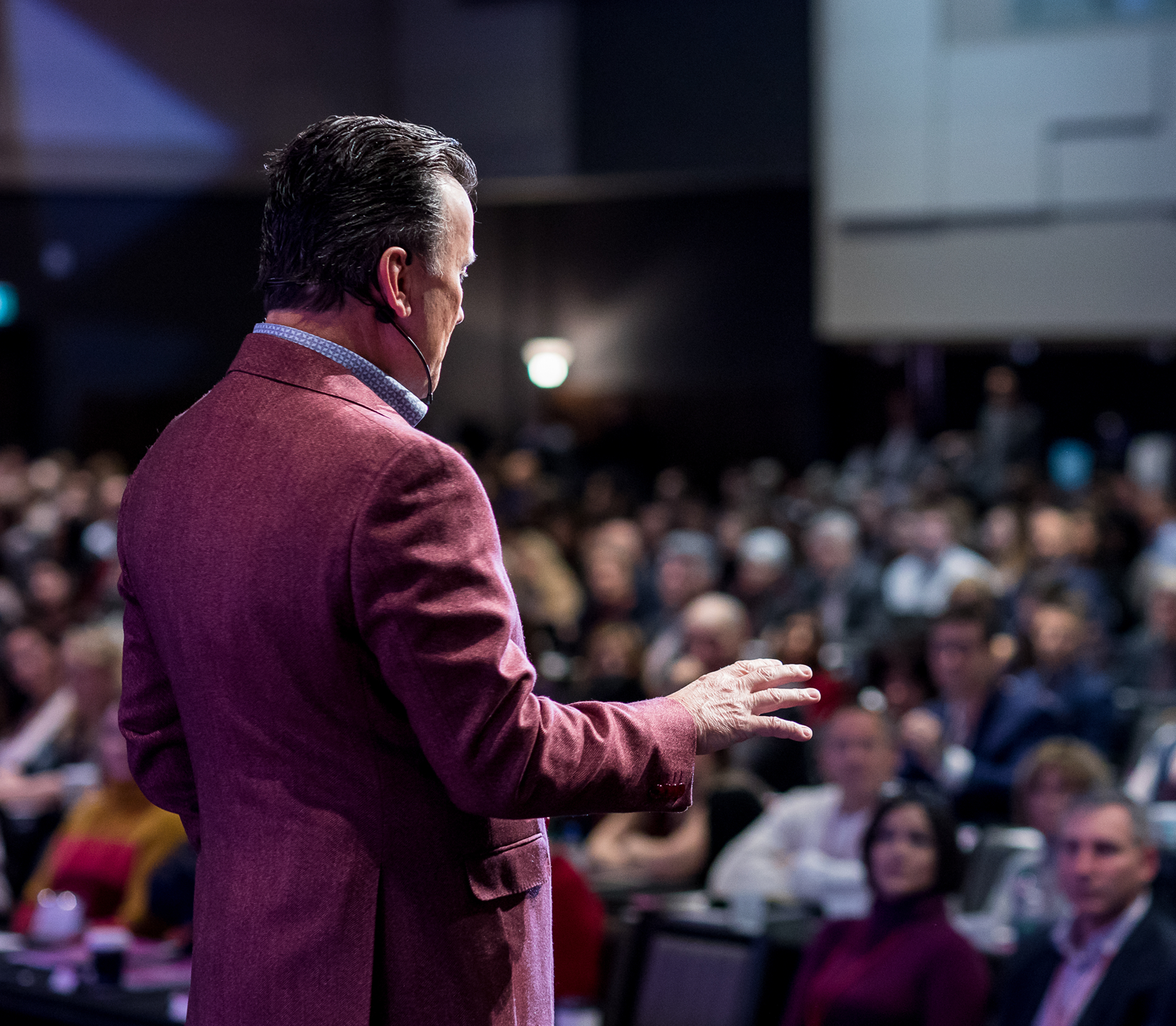 Speaker in red jacket presenting on stage to an audience