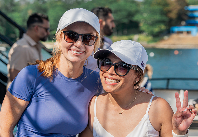 Two women in sunglasses and white caps smiling outdoors near the water.